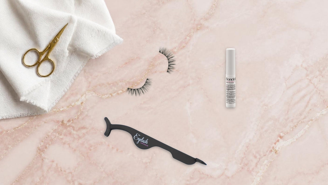 Strip lashes, Bondelle adhesive, applicator tool and small scissors laid out on a pink marble surface ready for application